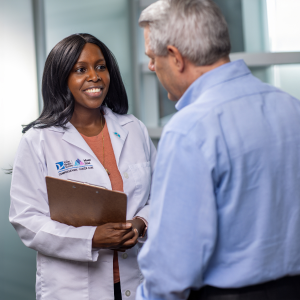 Female pulmonologist holding clipboard, smiling and speaking to male patient.