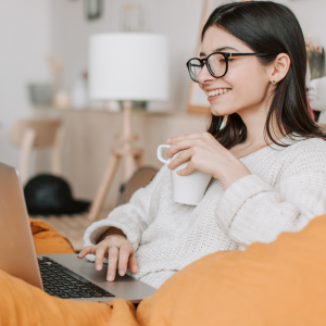 Woman smiling, holding a cup of tea watching something on a laptop.