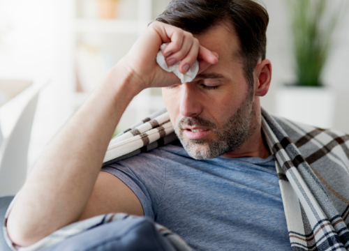 Man feeling unwell, with blanket over his shoulders and holding his forehead