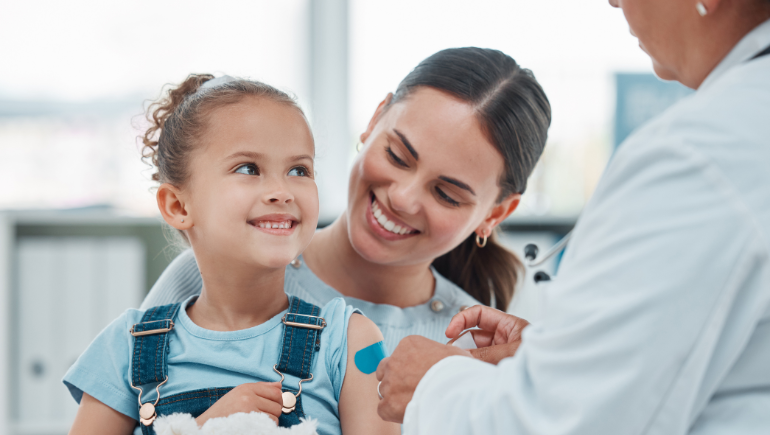 A doctor putting a band-aid on a child's arm after receiving a vaccine, with mom looking on