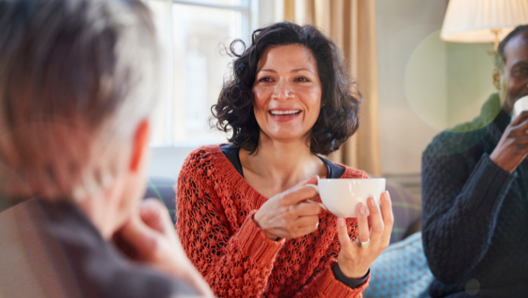 An older woman indoors enjoying a cup of coffee with friends