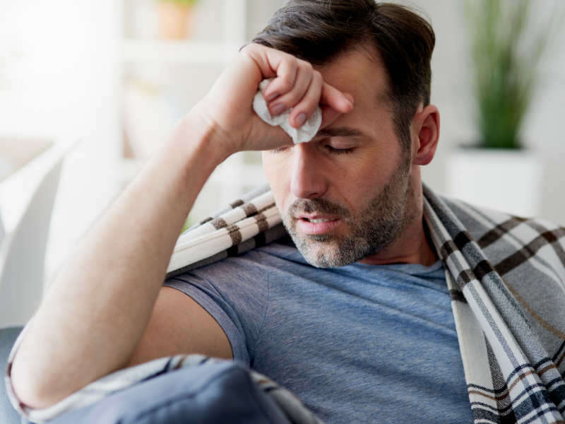 Man feeling unwell, with blanket over his shoulders and holding his forehead